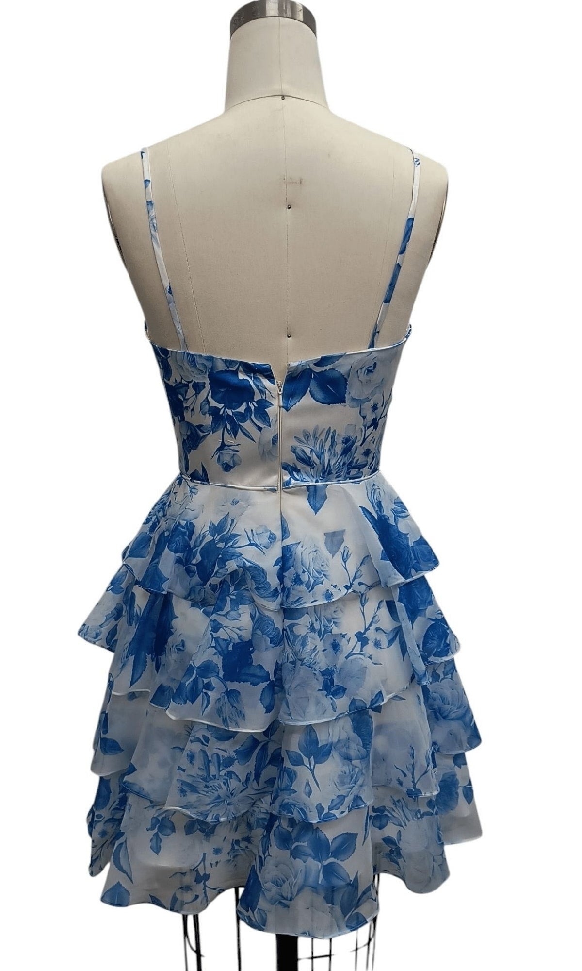 The Short Blue Print Hoco Dress: 12612 features thin straps, a blue floral print, and a tiered ruffle A-line skirtโshown from the back on a dress formโmaking it the perfect party dress for any occasion.